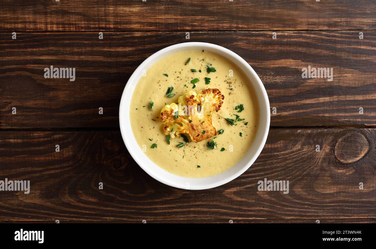 Zuppa di cavolfiore in ciotola su fondo di legno con spazio libero. Concetto di alimentazione vegetariana o sana. Vista dall'alto, base piatta Foto Stock