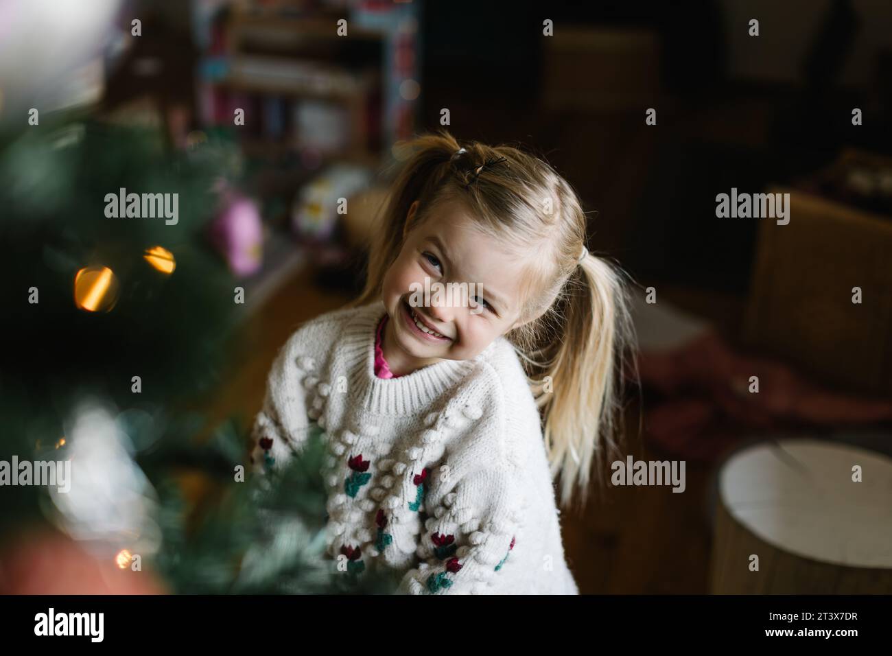 Un bambino allegro sorride davanti al radioso e scintillante albero di Natale Foto Stock