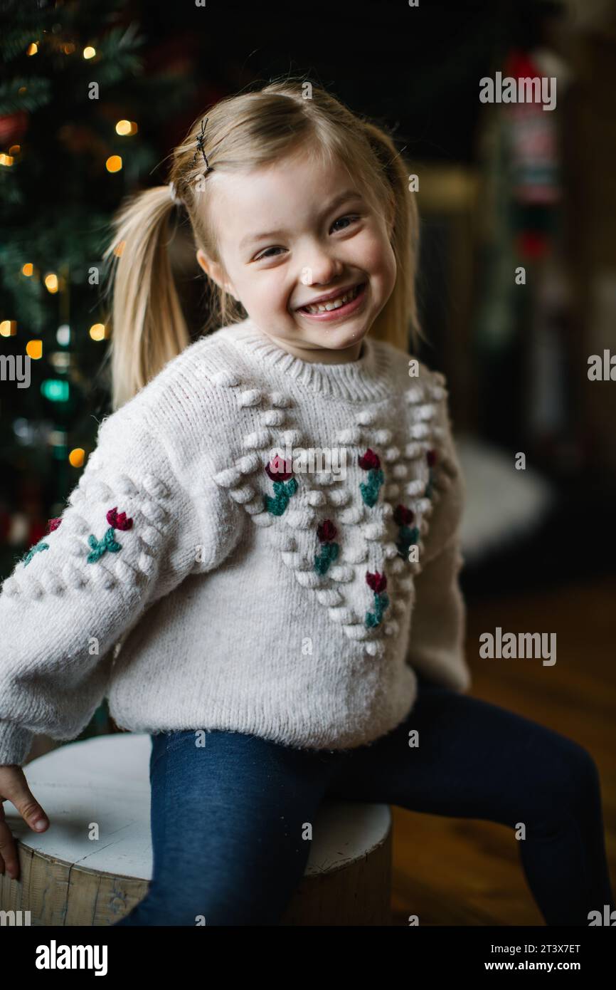 Un bambino allegro con un maglione di Natale posa, sorridente, vicino all'albero Foto Stock