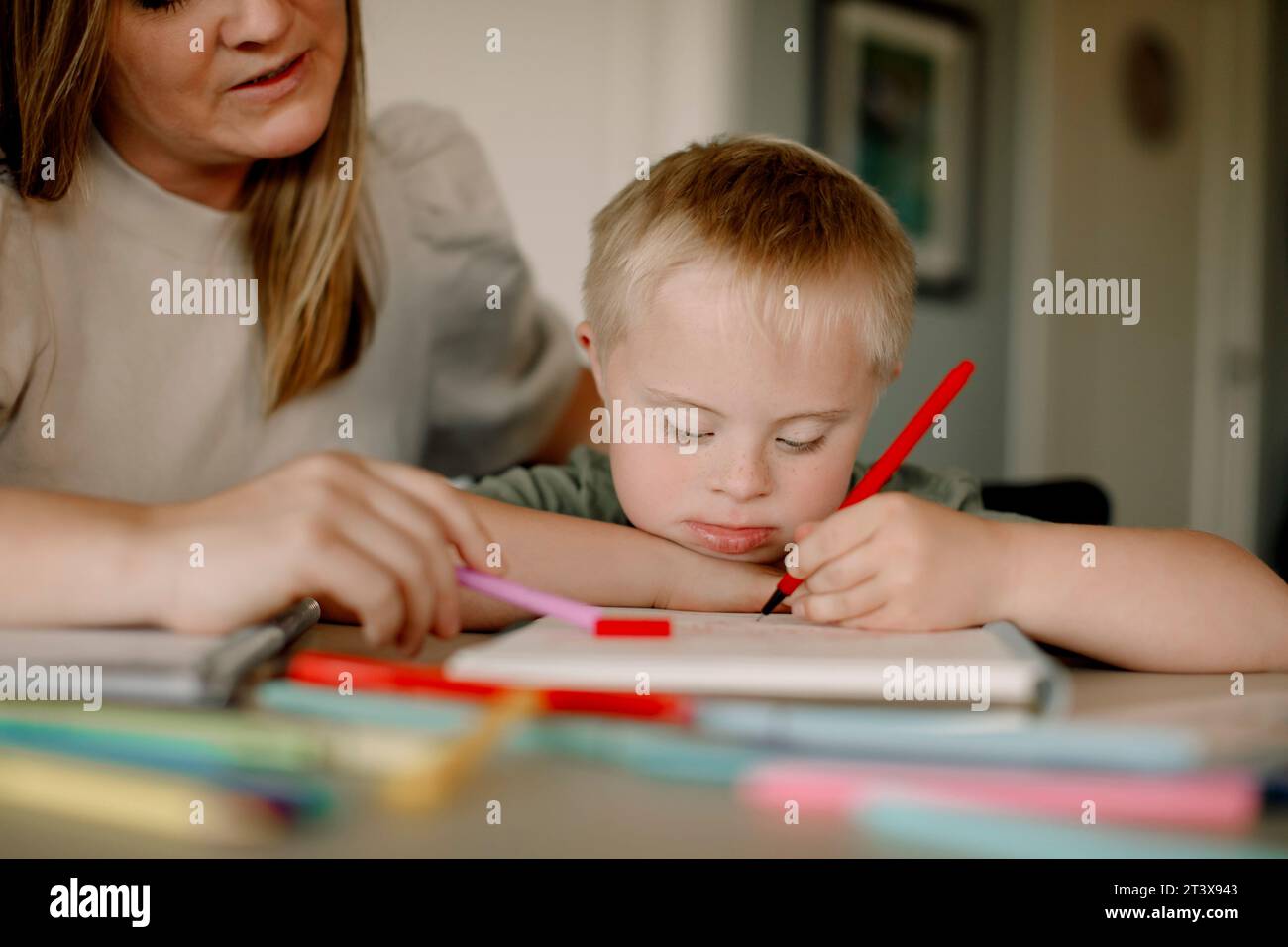 Ragazzo con sindrome di Down che disegna in libro da madre a casa Foto Stock