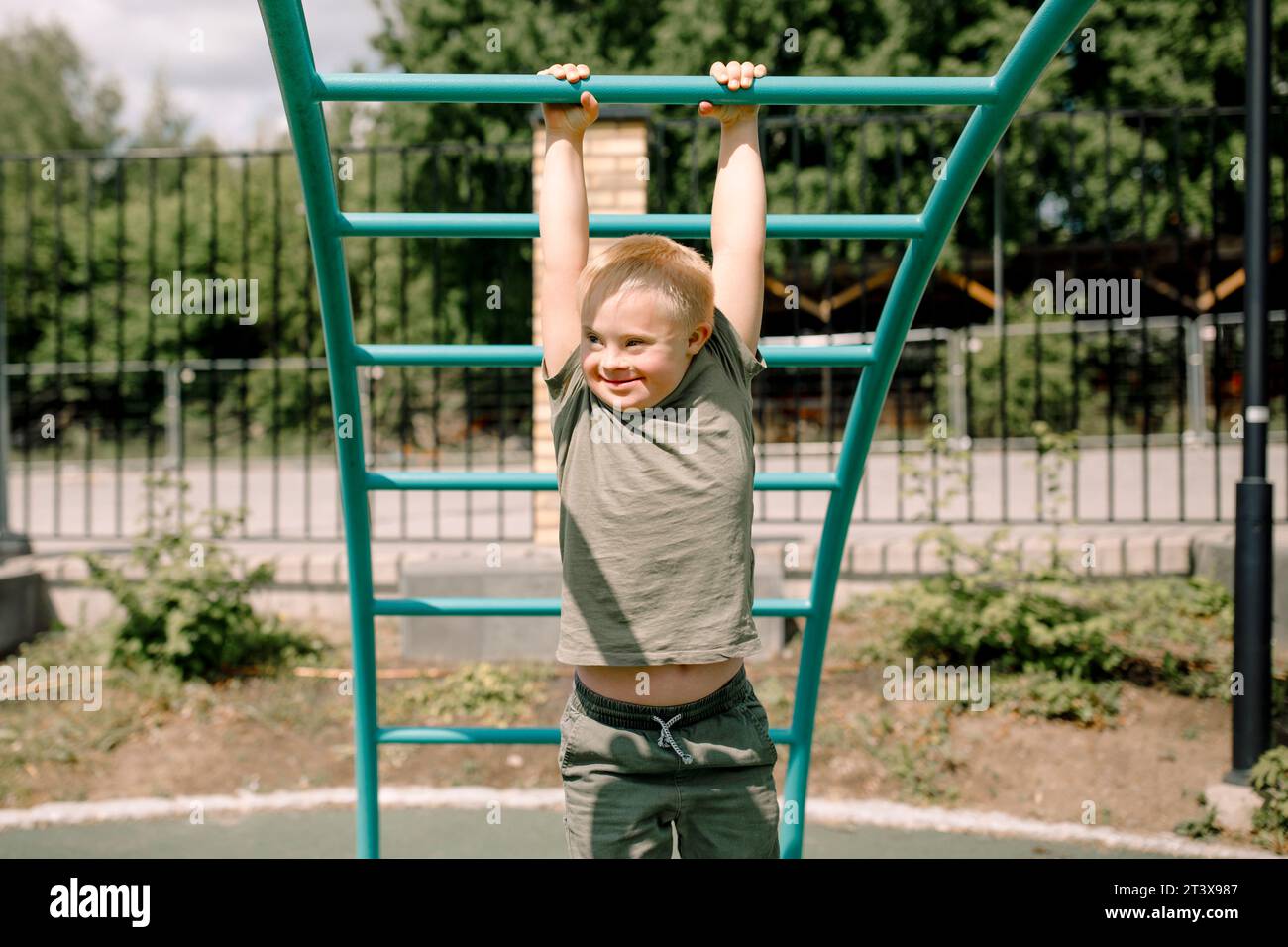Ragazzo sorridente con sindrome di Down appeso alla palestra della giungla al parco Foto Stock
