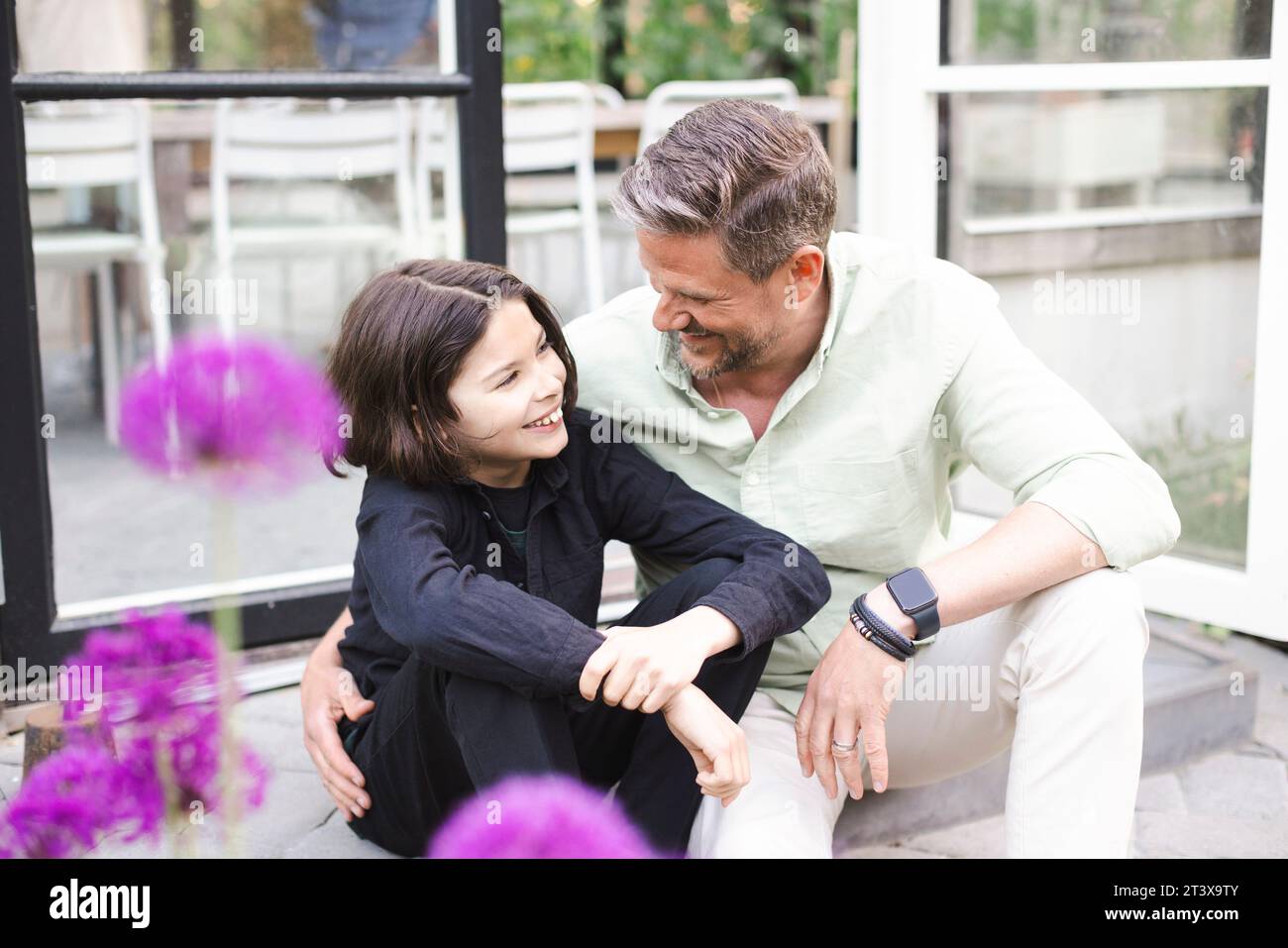 Padre e figlio felici che si guardano mentre sono seduti insieme sui gradini Foto Stock