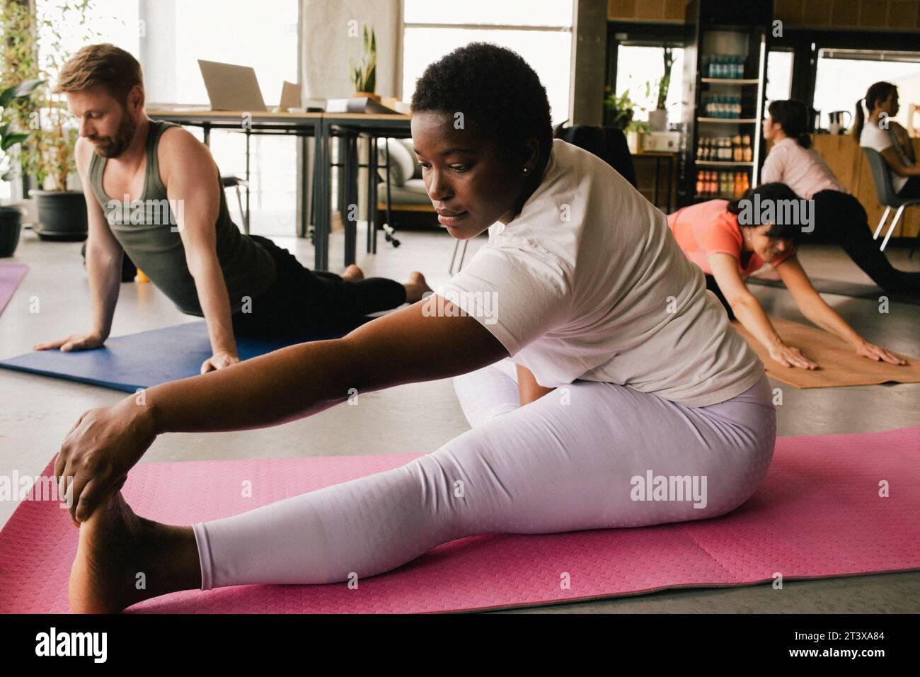 Donna d'affari flessibile che pratica yoga vicino a un uomo d'affari su tappetini per esercizi in ufficio Foto Stock