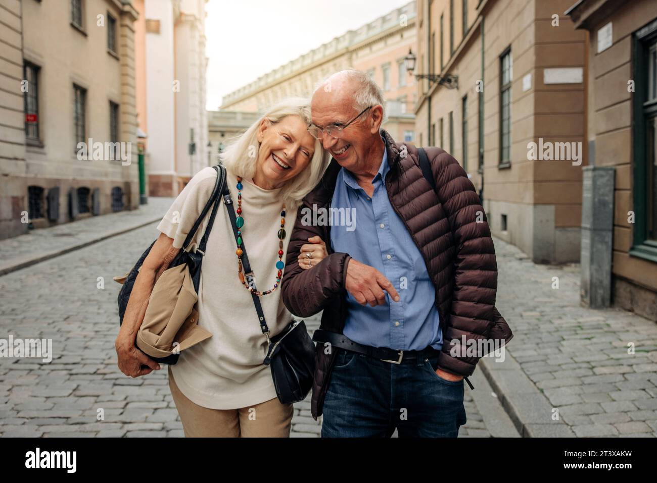 Felice coppia anziana in pensione con un braccio a braccetto che passeggia per la strada della città Foto Stock