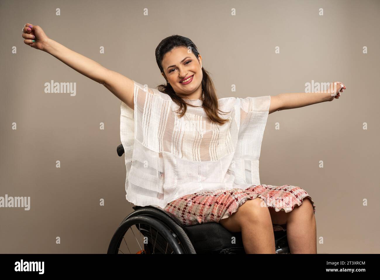 Un individuo vivace, che irradia gioia e positività, si allarga le braccia in un abbraccio aperto mentre si siede su una sedia a rotelle. Il suo sorriso e la sua postura conv Foto Stock