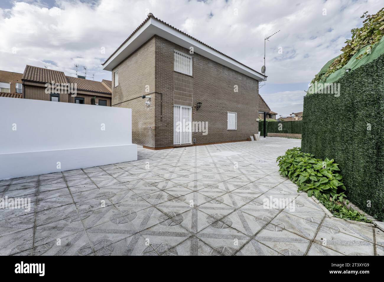 Trama con una casa residenziale a due piani per famiglie con pareti in mattoni marrone scuro, falegnameria esterna in metallo bianco, separatore di siepi sintetiche verdi Foto Stock