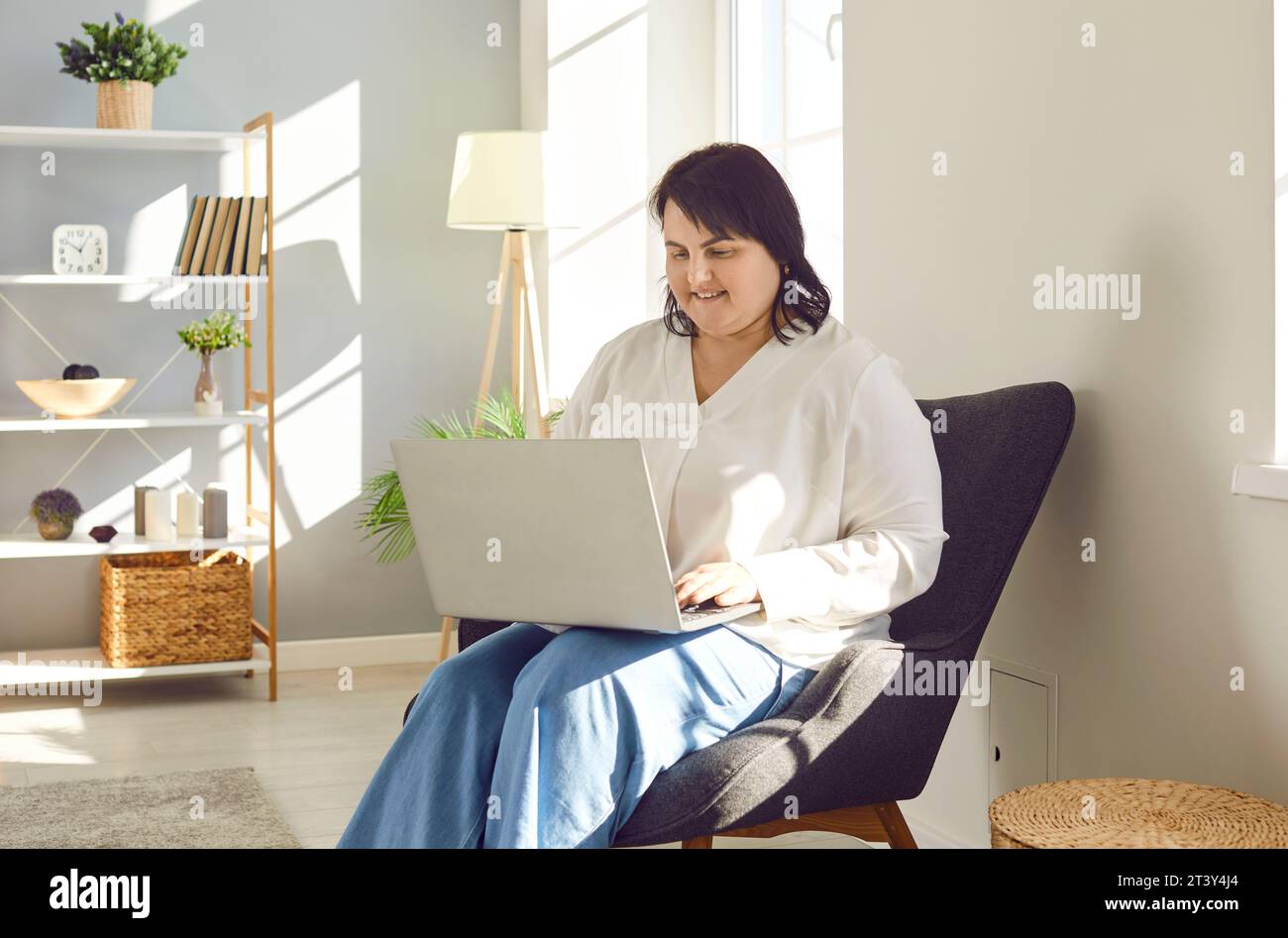 Donna obesa felice che si rilassa in sedia a casa, usa un computer portatile e guarda video Foto Stock