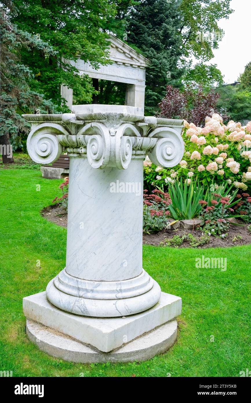 Toronto, Canada, Una piccola colonna di pietra che probabilmente regge una statua. L'antica struttura in marmo presenta dei fiori sullo sfondo. (Foto di: Roberto Macha Foto Stock