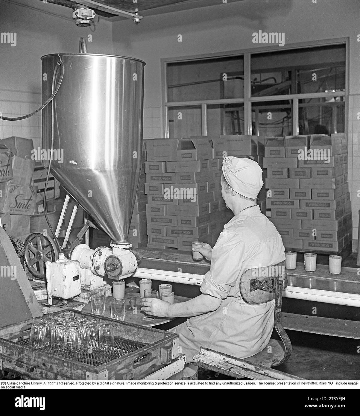 Lavori negli anni '1940 Interni delle fabbriche della società alimentare Winborg, dove una dipendente donna siede in una macchina che riempie vasetti di vetro che poi posiziona su un nastro trasportatore in modo che il vaso arrivi al lavoratore successivo che si avvita su un coperchio. Svezia 1949. Kristoffersson rif. AM2-4 Foto Stock