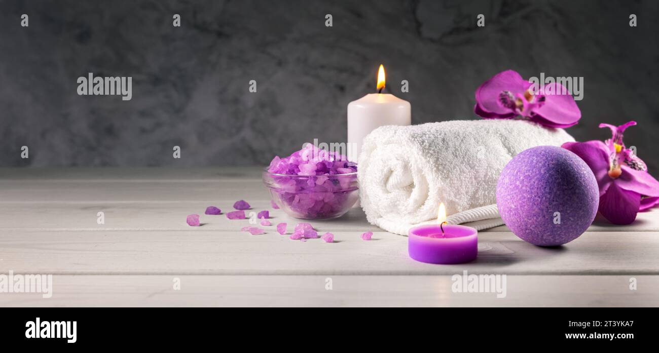 bomba da bagno viola, cristalli di sale marino, asciugamano e candele profumate su un tavolo di legno. centro benessere e spa. striscione con spazio per la copia Foto Stock