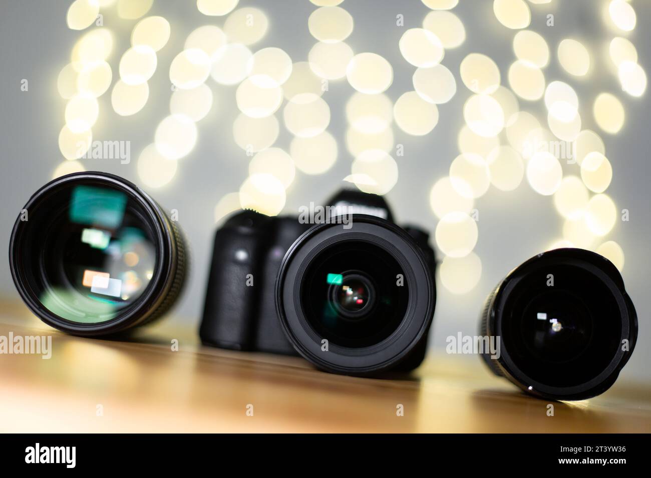 Fotocamera digitale e obiettivo professionale su un tavolo in legno, vista frontale inclinata. Sfondo fotografico straordinario con bokeh giallo Foto Stock