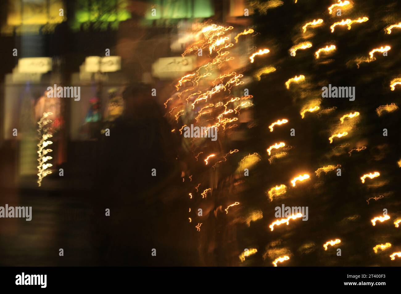 Atmosfera natalizia intima, sfocata e astratta, concetto di mondo confuso. Figura sfocata della persona che cammina lungo una strada illuminata e luminosa con luci natalizie Foto Stock