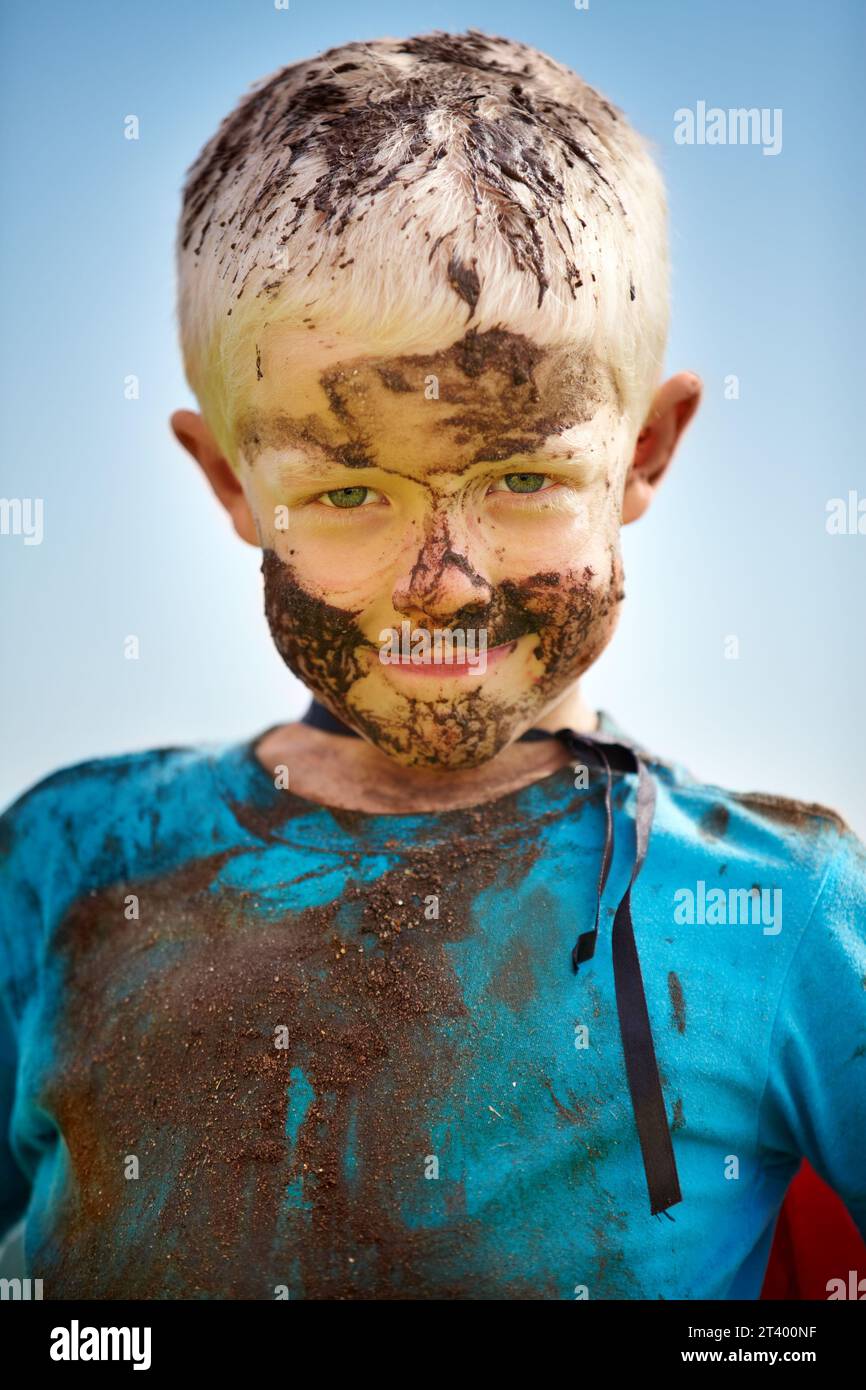 Bambino, bambino e fango sul viso con il sorriso dal gioco, sporco o felicità in estate o in acqua. Ragazzo, persona e ritratto con soddisfazione per disordine Foto Stock