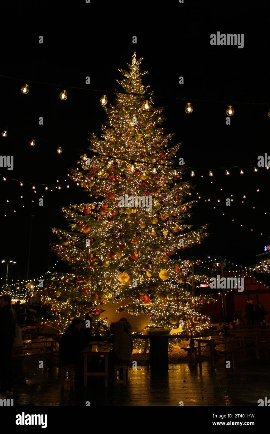 Vero, completamente decorato con ornamenti oro e rosso o bauble, albero natalizio invernale incastonato con luci delle fate d'oro gialle di notte in un mercato Foto Stock