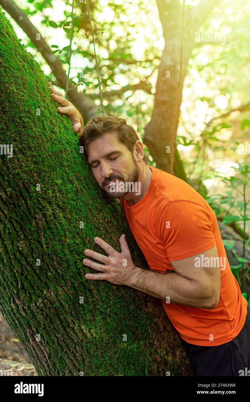 Un uomo con una t-shirt arancione che abbraccia un albero. Amore per la natura. Tutela dell'ambiente e rispetto delle piante e della vegetazione Foto Stock