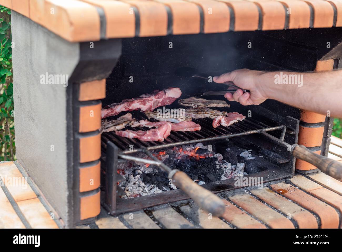 Grigliare la carne su un barbecue in mattoni con una brace luminosa. Loins di maiale, costolette e costolette che cucinano alla griglia Foto Stock
