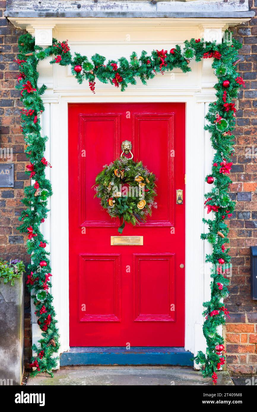 BUCKINGHAMSHIRE, Regno Unito - 26 dicembre 2022. Corona di Natale e ghirlanda sulla tradizionale porta d'ingresso dipinta di rosso, Regno Unito Foto Stock