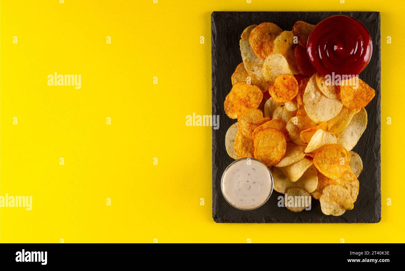 Patatine fritte finemente affettate e condite con salsa bianca cremosa e rossa salata su sfondo giallo Foto Stock