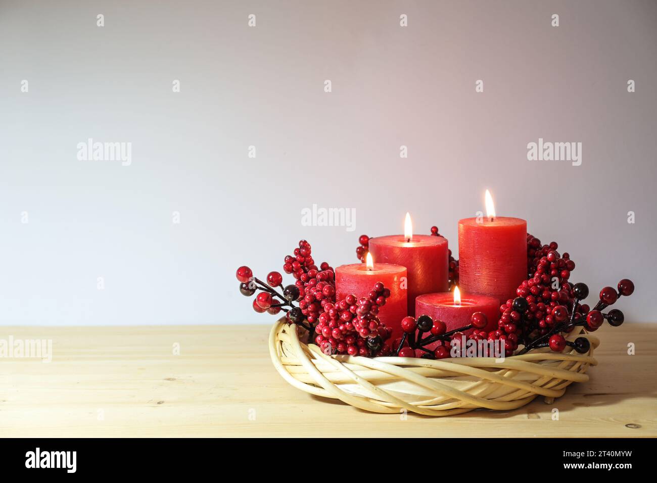 Quarto avvento con quattro candele rosse, tutte illuminate, decorate in una corona di vimini di salice naturale con bacche artificiali, sistemazione per le vacanze, copia Foto Stock