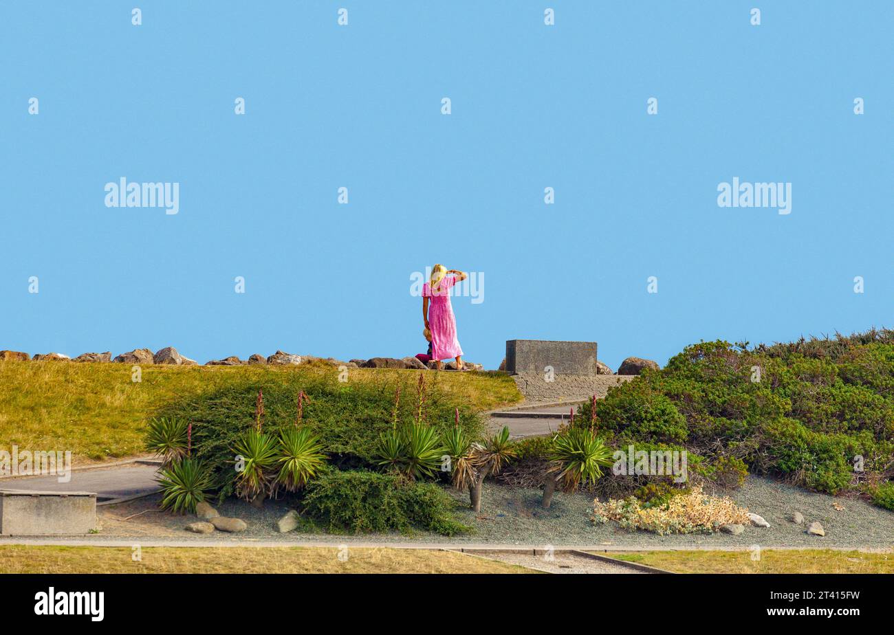 Donna con un colorato abito rosa in piedi con un bambino piccolo sul Cardiff Barrage, che si distingue contro un cielo blu Foto Stock