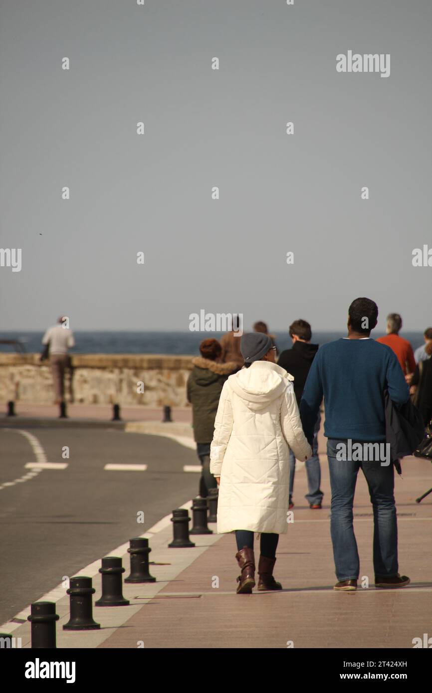 Un gruppo di persone fa una passeggiata lungo una passerella, godendo della tranquilla vista di San Sebastian Foto Stock