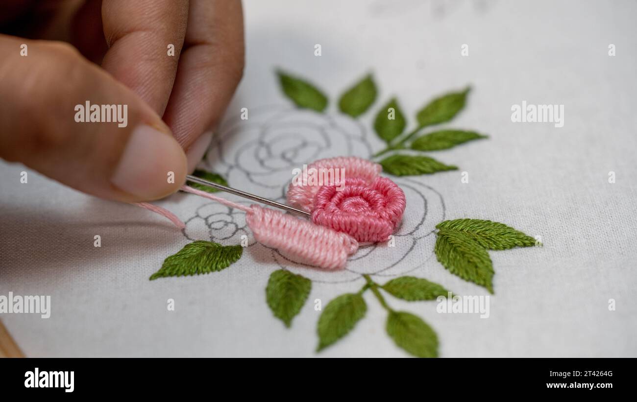 Ricamo con cuciture a mano e rosa su sfondo bianco. Foto Stock