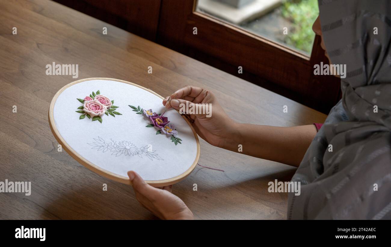 Primo piano di una donna che ricama fiori su un cerchio di legno a casa Foto Stock