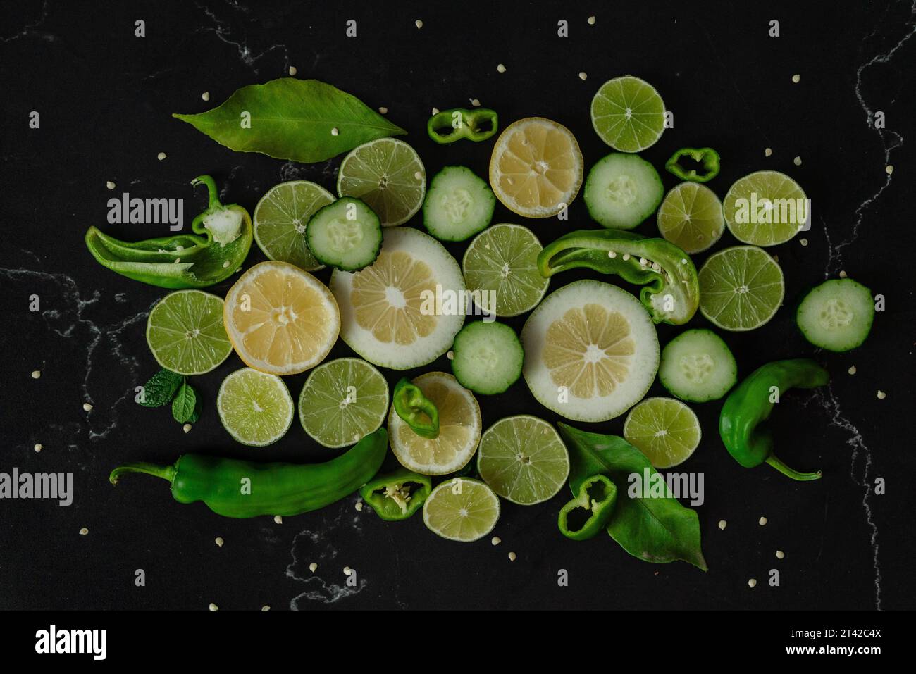 Un primo piano di una vivace gamma di ingredienti, tra cui fette di lime, foglie verdi e fagioli di zucchero, disposti su sfondo nero Foto Stock