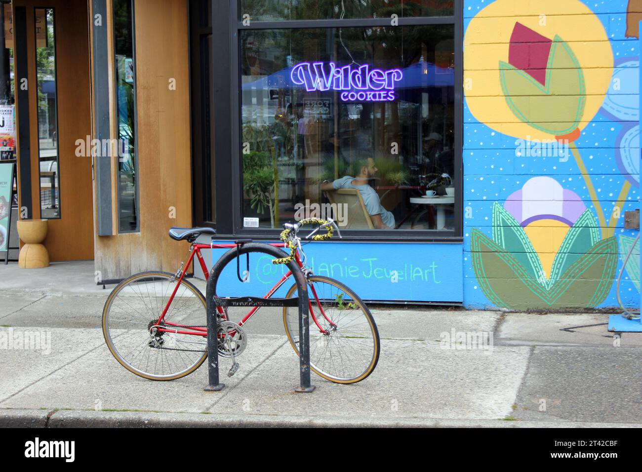 Una bicicletta rossa bloccata saldamente su un palo all'esterno di un edificio blu e verde vibrante Foto Stock