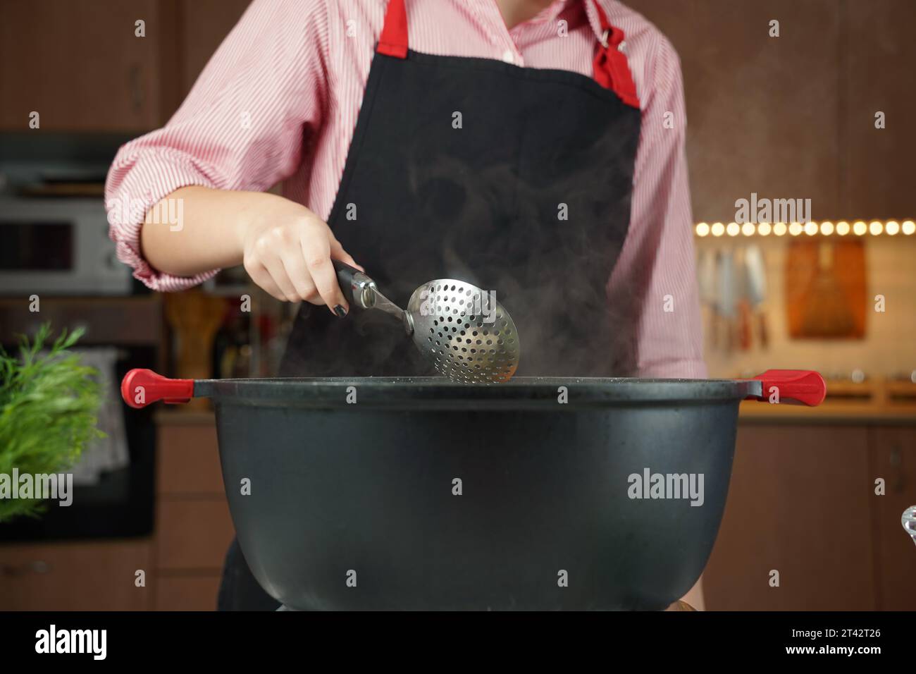 Donna con mestolo che cucina in pentola nera con acqua bollente . Cuocere a vapore sul recipiente Foto Stock