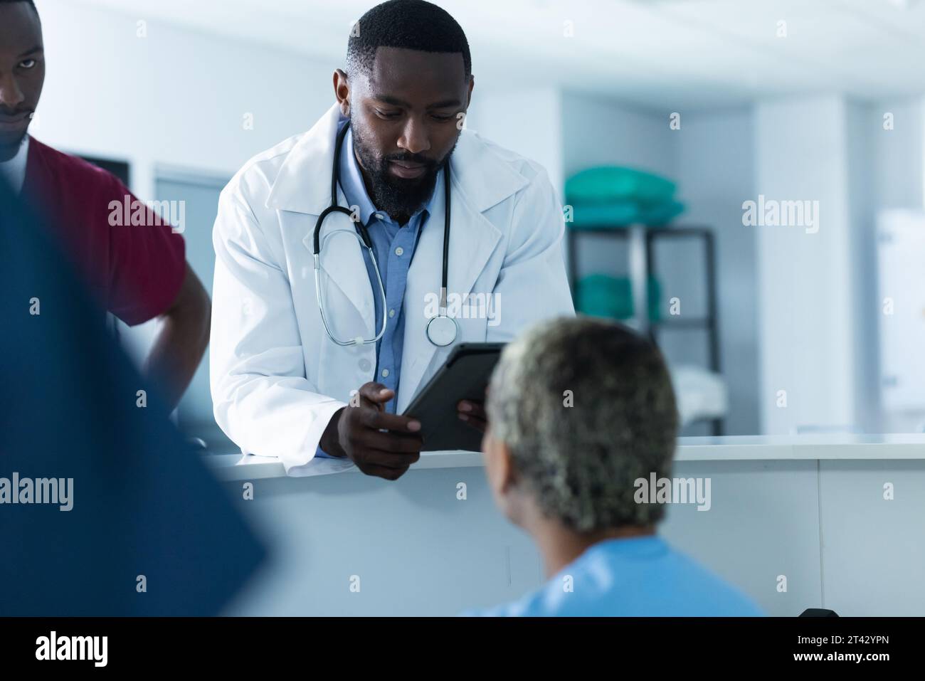 Diversi medici maschi discutono di lavoro, utilizzando tablet alla reception in ospedale Foto Stock