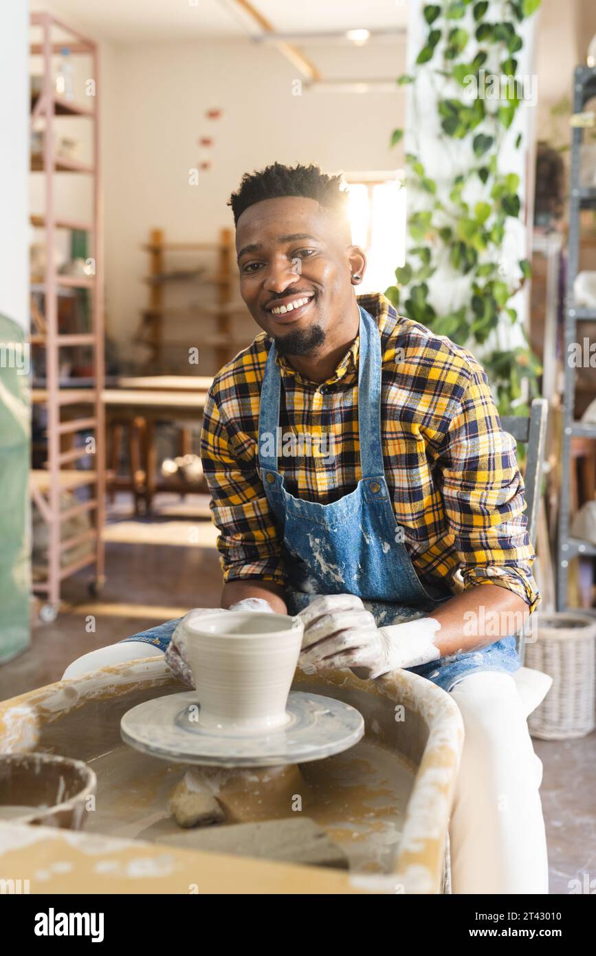 Felice ceramista afro-americano che lavora su un vaso di argilla usando la ruota di potter nello studio di ceramica Foto Stock