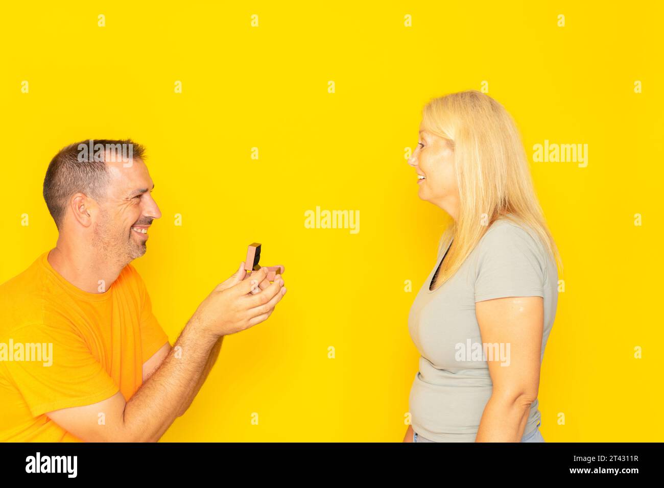 Un uomo che si propone ad una donna che sembra felice e sorpreso. Concetto di amore e matrimonio. sfondo giallo isolato. Concetto romantico, comprare gioielli Foto Stock