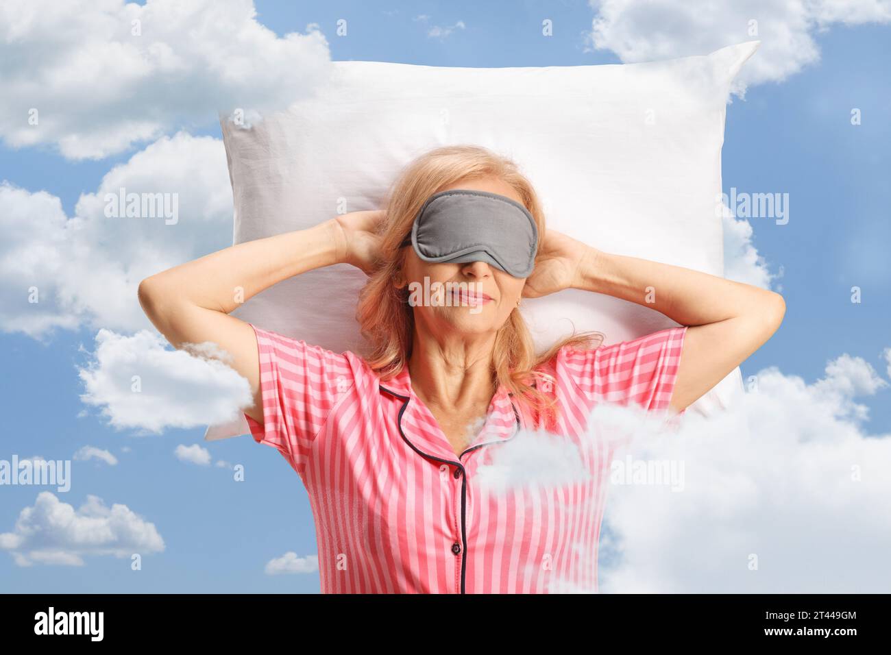 Donna in pigiama con una maschera sugli occhi che dorme su un cuscino tra le nuvole e il cielo blu Foto Stock