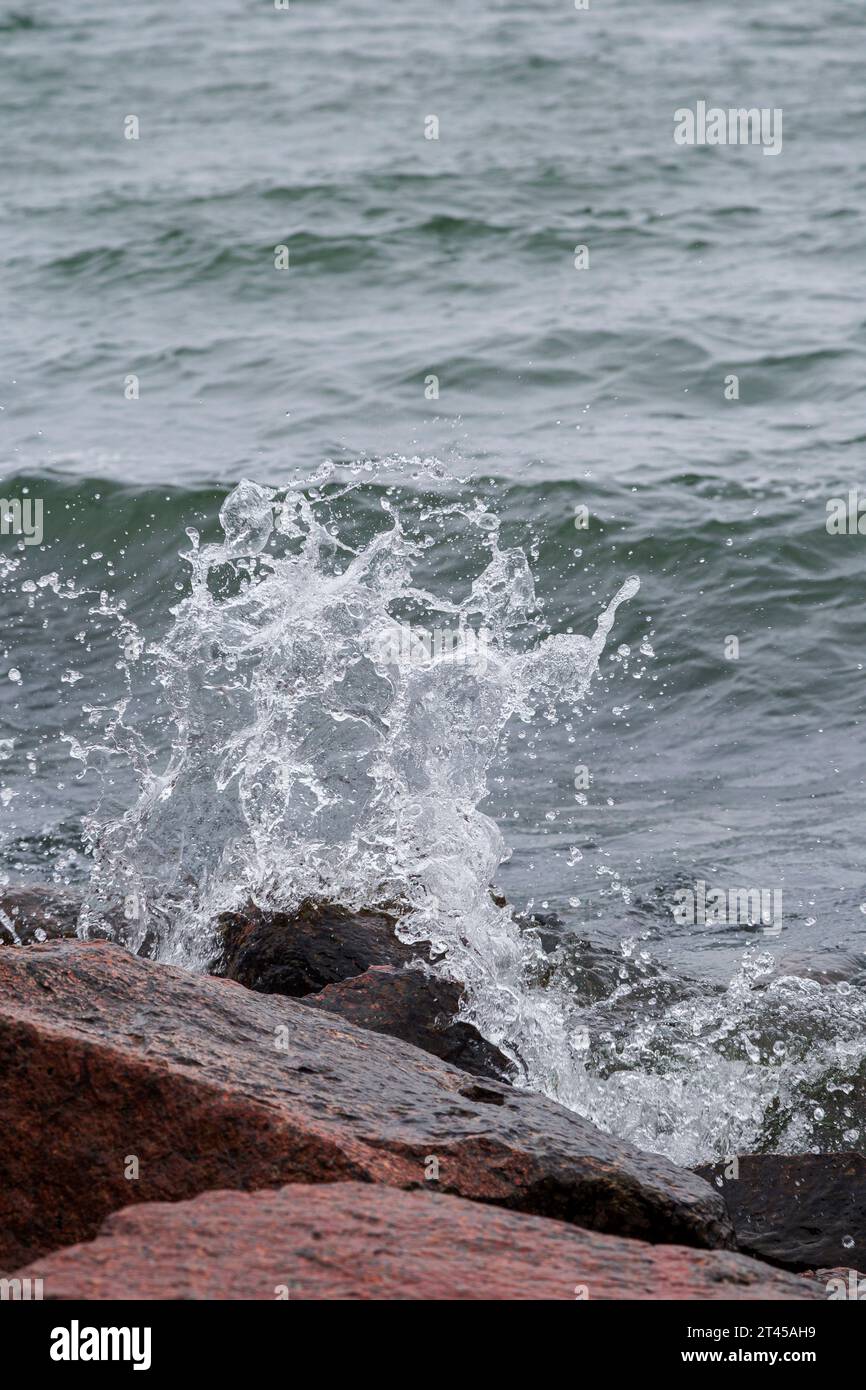 Primo piano dello spruzzo di una piccola onda che si schianta sulle rocce. Foto Stock