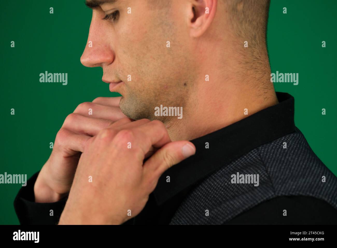 Primo piano delle mani di un uomo che raddrizza una camicia nera, regala un giubbotto classico, spalle da lati diversi, imposta tre foto su sfondo verde primo piano cromakey, capelli scuri Foto Stock