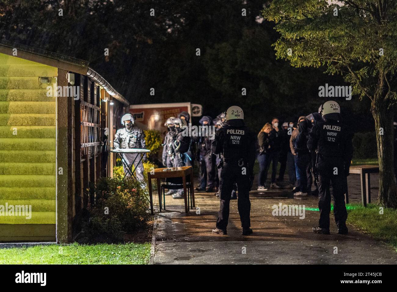 Gelsenkirchen, Germania. 28 ottobre 2023. Gli agenti di polizia si trovano di fronte alla clubhouse di un giardino di assegnazione, mentre i partecipanti a un concerto di destra sono guidati uno ad uno e presi per l'identificazione. La polizia ha posto fine a un evento di sospetti sostenitori della scena di destra a Gelsenkirchen. Secondo i primi risultati della polizia, circa 80 persone si erano riunite per un concerto in un circolo di un giardino di assegnazione il sabato sera. Credito: Christoph Reichwein/dpa/Alamy Live News Foto Stock