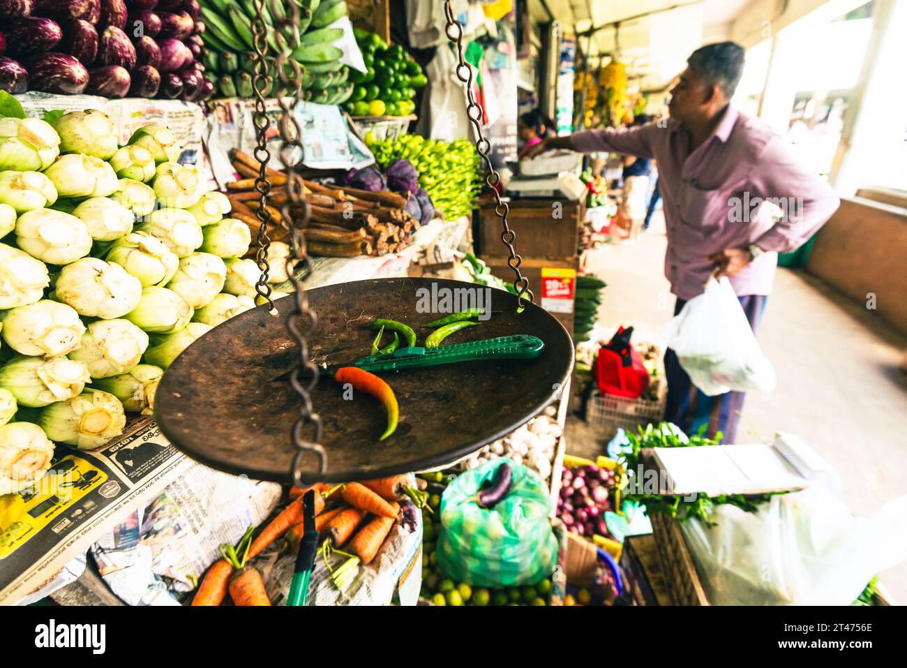 I Chilis sono su una bilancia mentre un uomo preleva alcune verdure in una bancarella di frutta e verdura nel mercato di Kandy in Sri Lanka Foto Stock