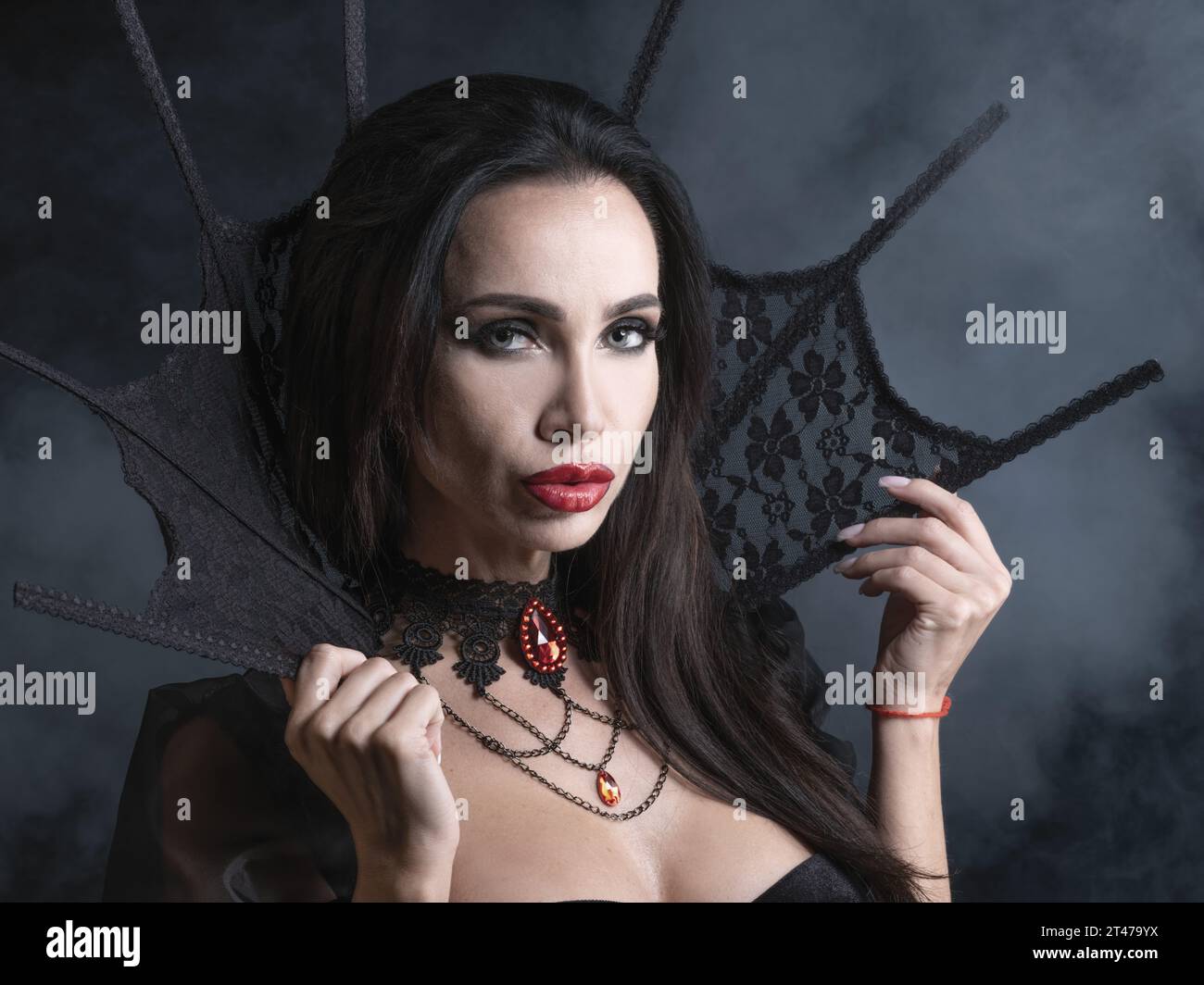 Bella giovane donna come vampiro sexy in abito nero con colletto alto e gemma rosso gioielli - ritratto di Halloween Foto Stock