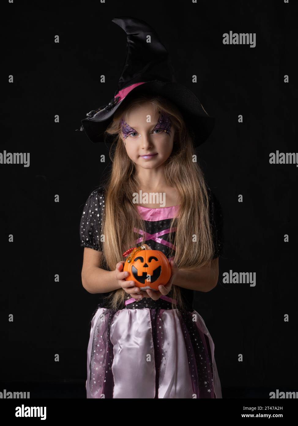 Cute ragazza strega di Halloween in costume fantasy che tiene il secchio di zucca con vermi caramelle, isolato su sfondo nero Foto Stock