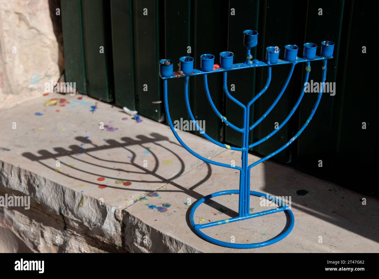 Una menora di Hanukkah blu e metallica getta un'ombra su un muro di pietra fuori da una casa di Gerusalemme durante il giorno durante il Festival delle luci in Israele. Foto Stock