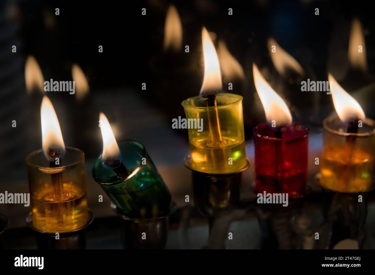 Le fiale di vetro multicolore trattengono olio e stoppini brucianti in una menorah luminosa durante il festival ebraico di Hanukkah. Foto Stock