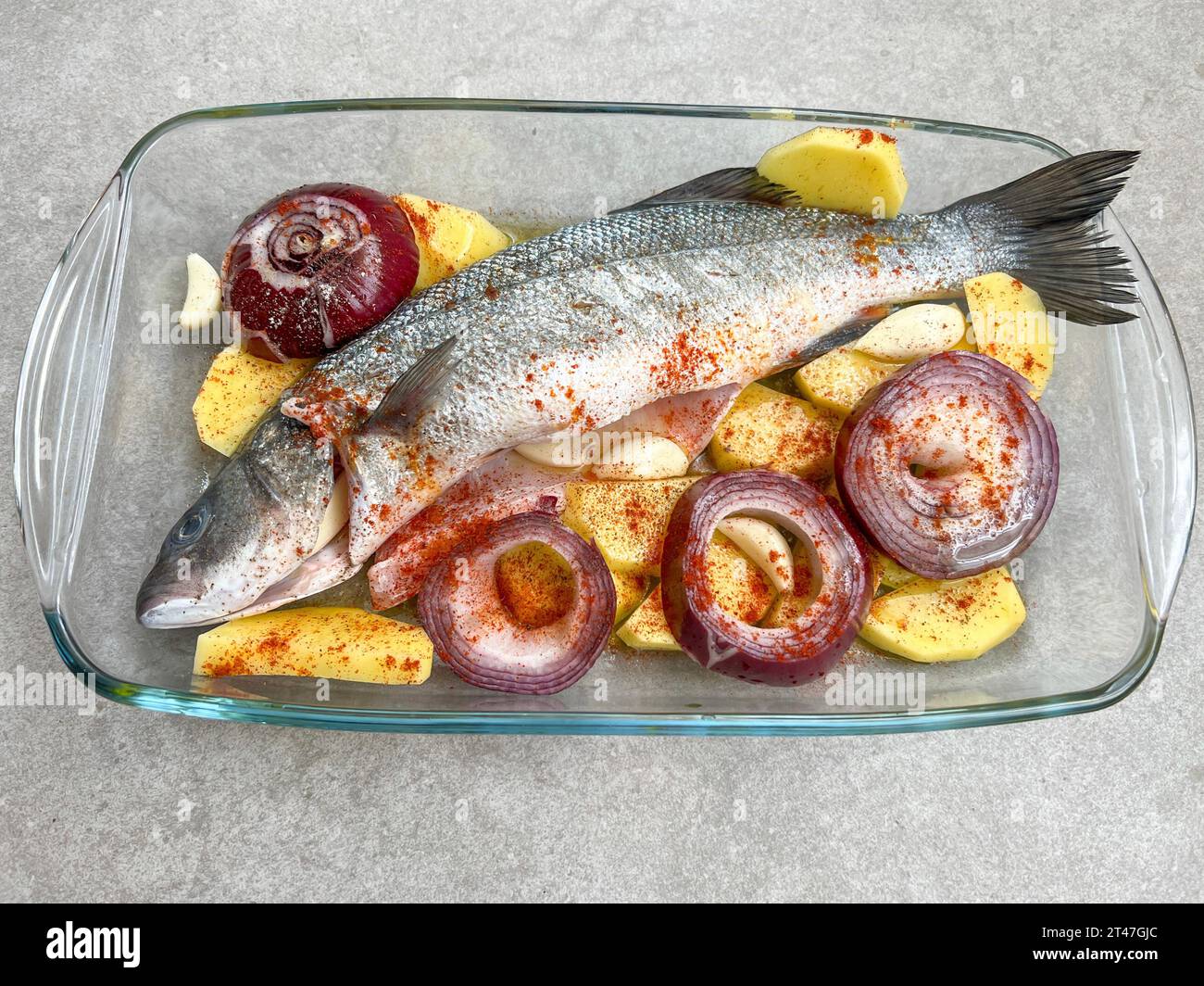 Pesce spigola crudo preparato con olio d'oliva e spezie da cuocere con patate e cipolle. preparazione di frutti di mare da cuocere nel forno. pesce crudo e vegetabl Foto Stock