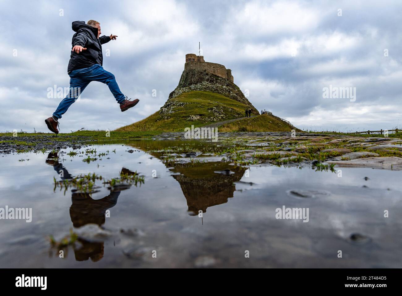 Holy Isle, Regno Unito. 28 ottobre 2023 nella foto: I corridori saltano su pozzanghere vicino al castello di Lindisfarne sulla Holy Isle nel Northumberland. Credito: Foto Stock