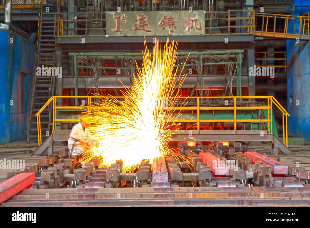 TANGSHAN - 20 GIUGNO: Lavoratori che tagliano lingotti d'acciaio dietro la macchina di colata continua in acciaieria, il 20 giugno 2014, Tangshan City, provincia di Hebei, Foto Stock