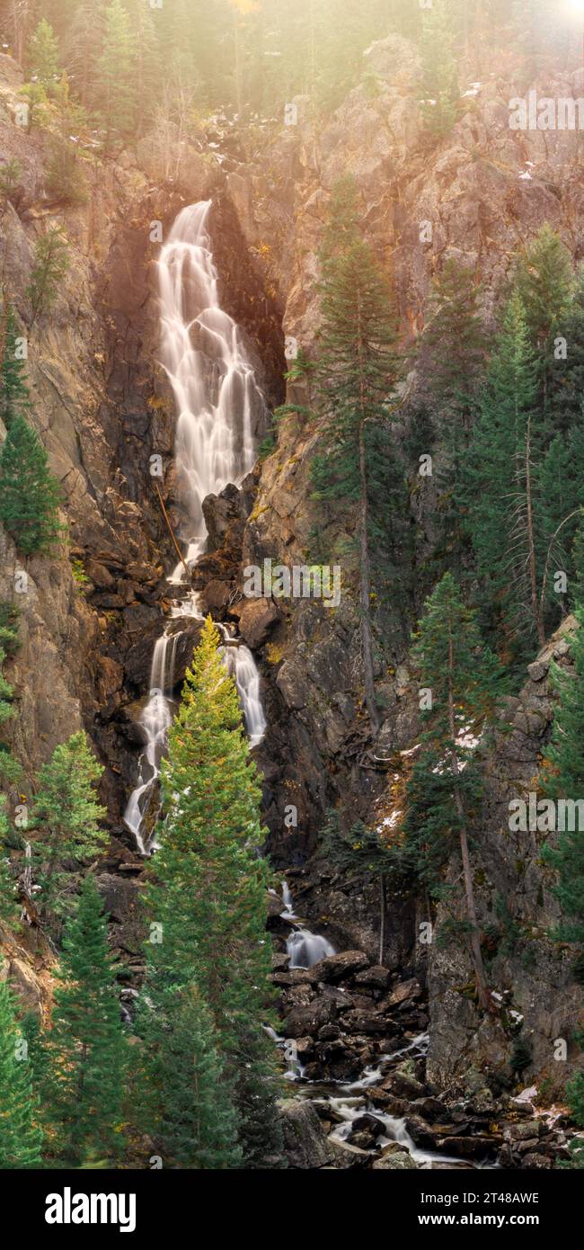 Una lunga foto di Fish Creek Falls in Colorado con molti alberi sempreverdi e un punto luminoso appena fuori dall'inquadratura. Acqua setosa e calmante Foto Stock