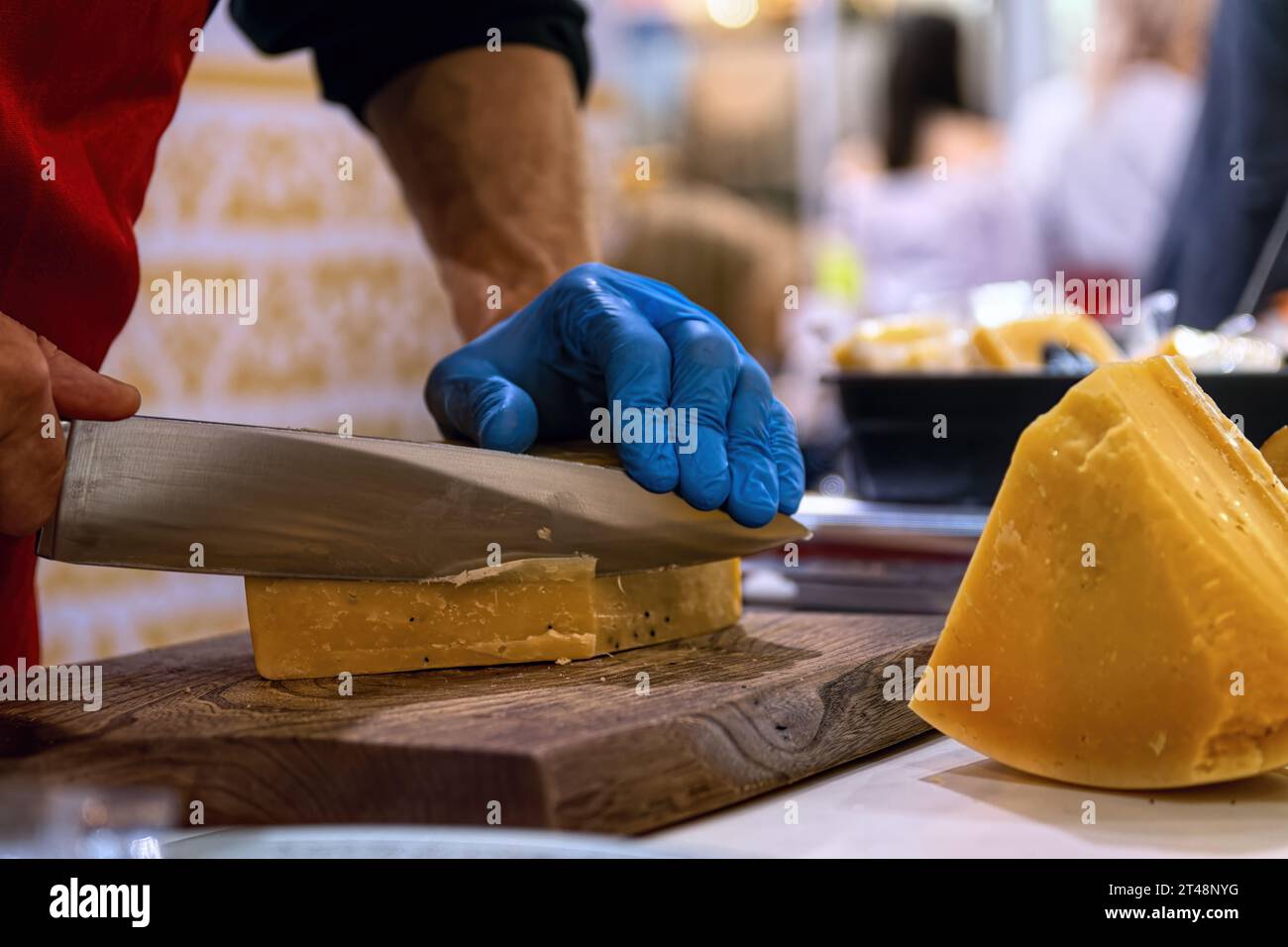 Venditore di affettare il formaggio su un tagliere di legno. Negozio di formaggi. Foto Stock