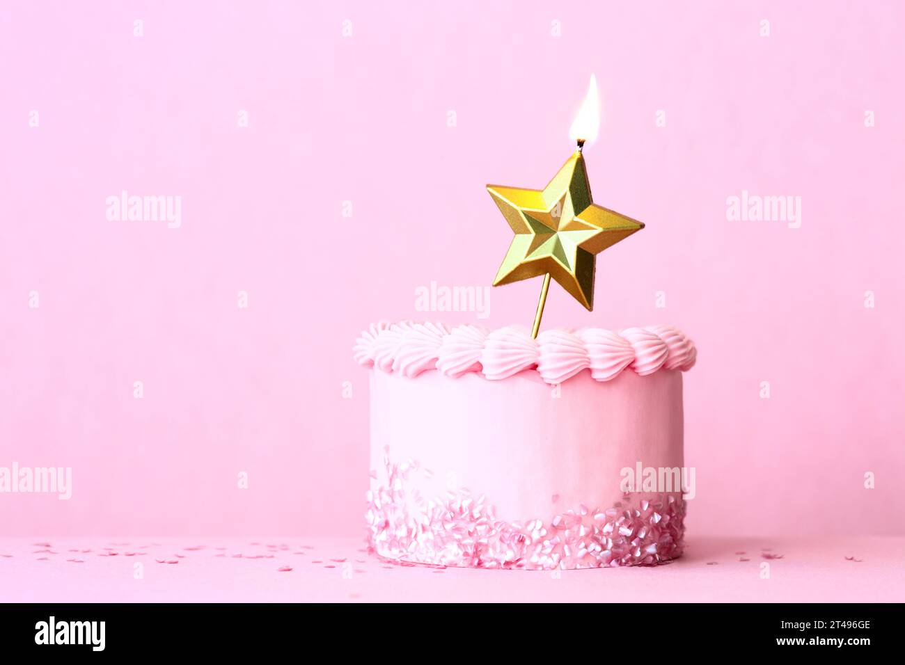 Torta di compleanno rosa smerigliata con una candela di compleanno Gold Star e spruzzi a forma di cuore su un semplice sfondo rosa Foto Stock