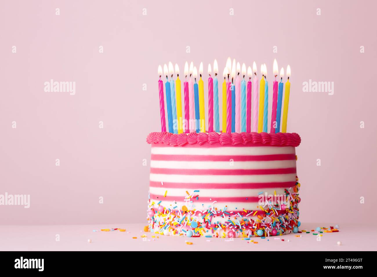 Torta di compleanno decorata con crema di burro a righe rosa e bianche e tante candele di compleanno su sfondo rosa Foto Stock