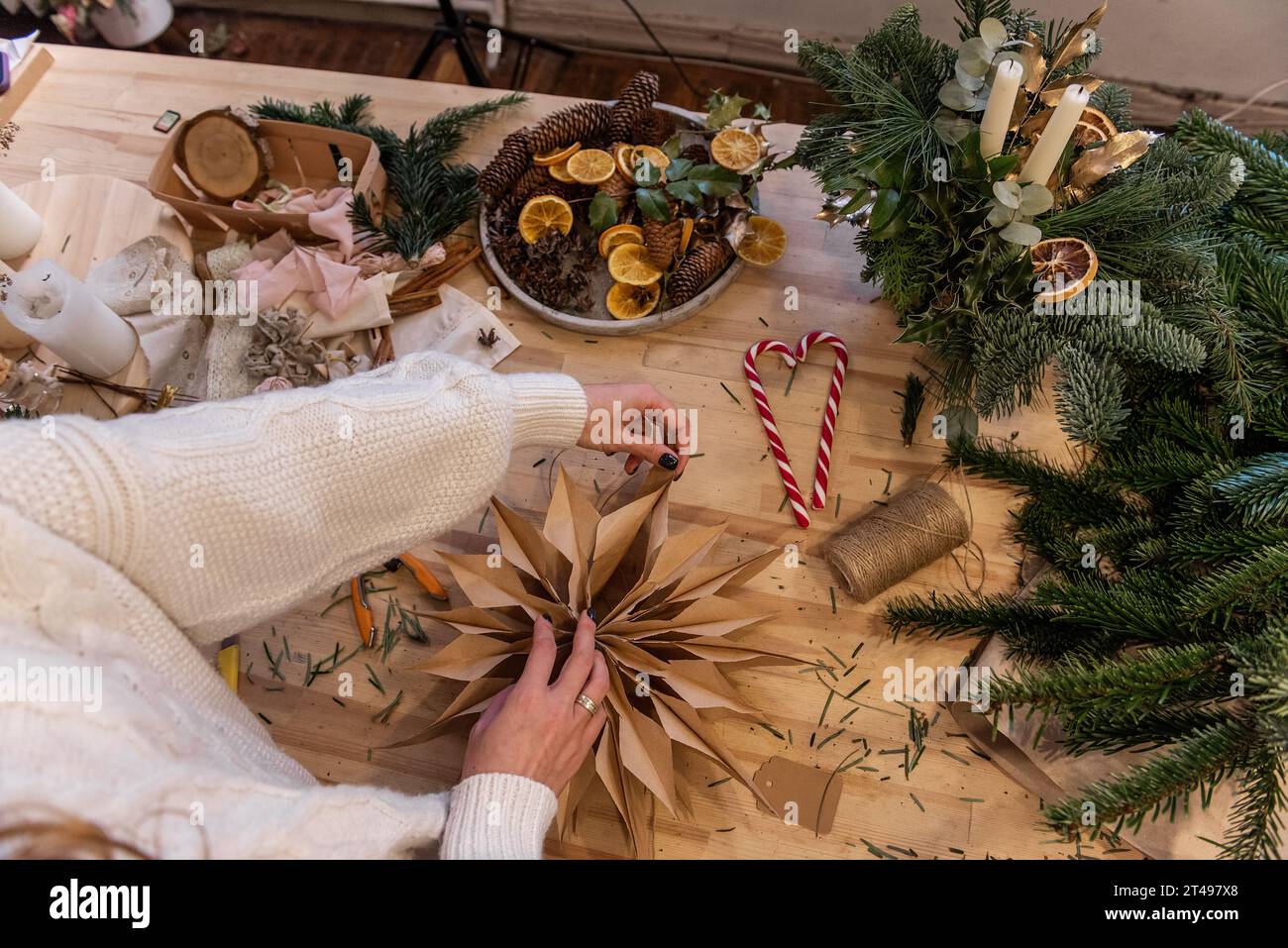 La ragazza senza volto sta regolando la stella in carta artigianale fatta con le proprie mani su un tavolo di legno. Decorazioni naturali per la casa per Natale. Intorno alle stelle ci sono candele Foto Stock